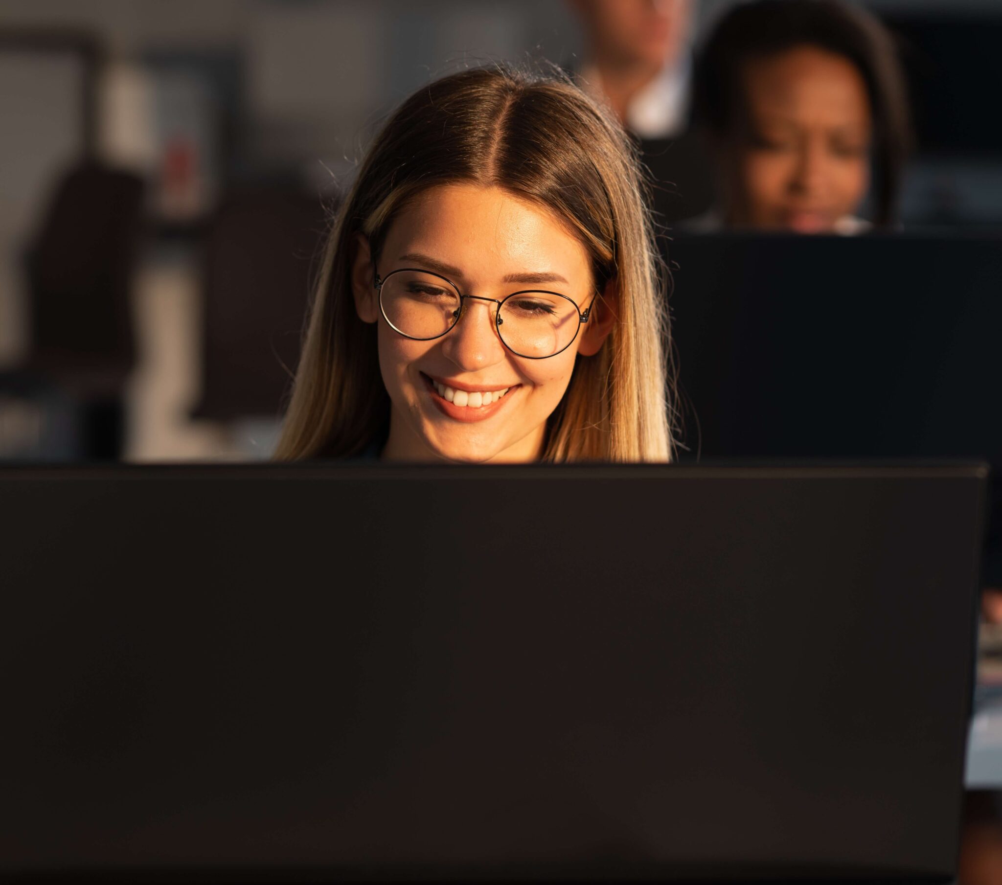A woman smiling while working behind a computer screen.